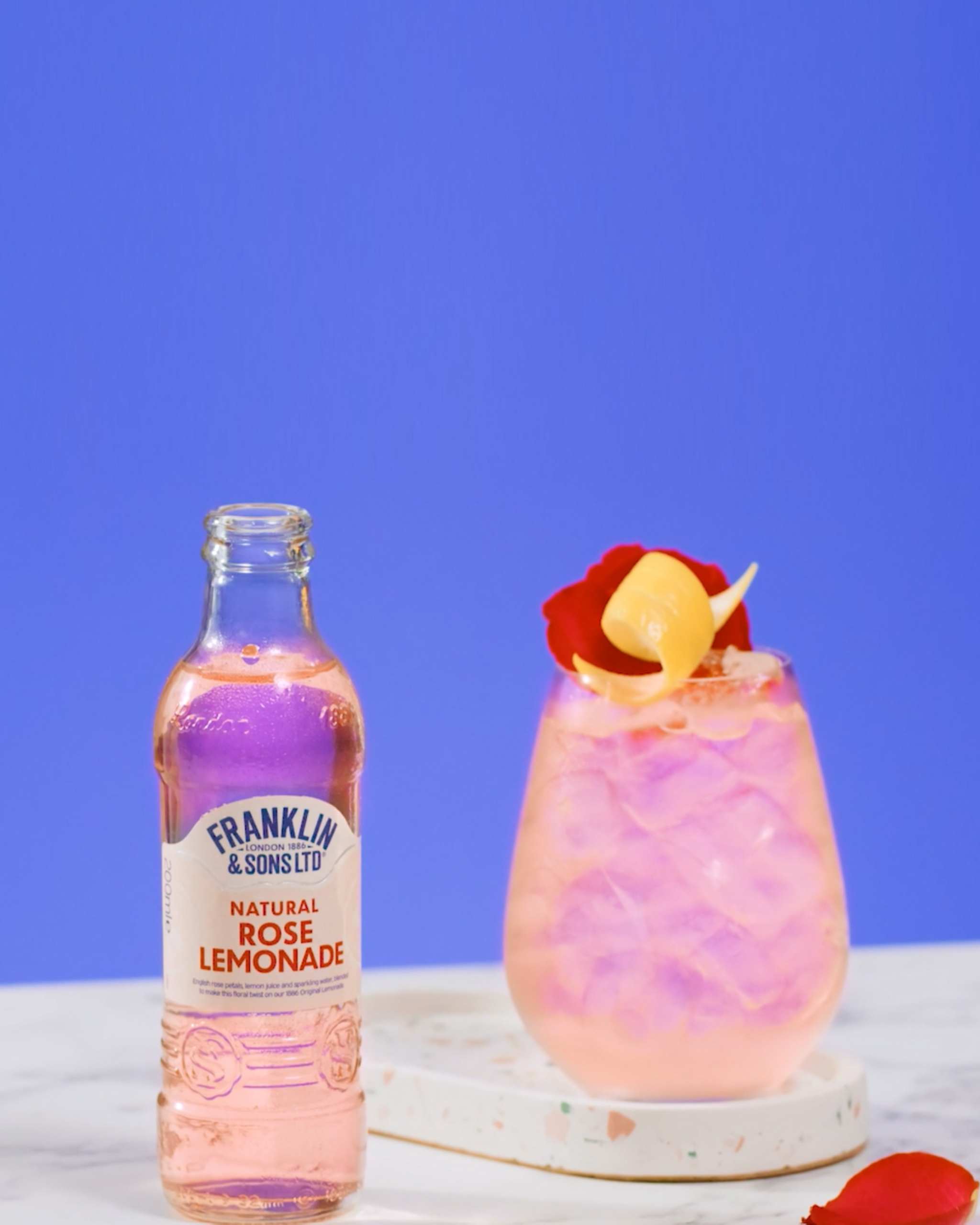 Franklin & Sons Rose Tom Collins cocktail next to a bottle of Natural Rose Lemonade